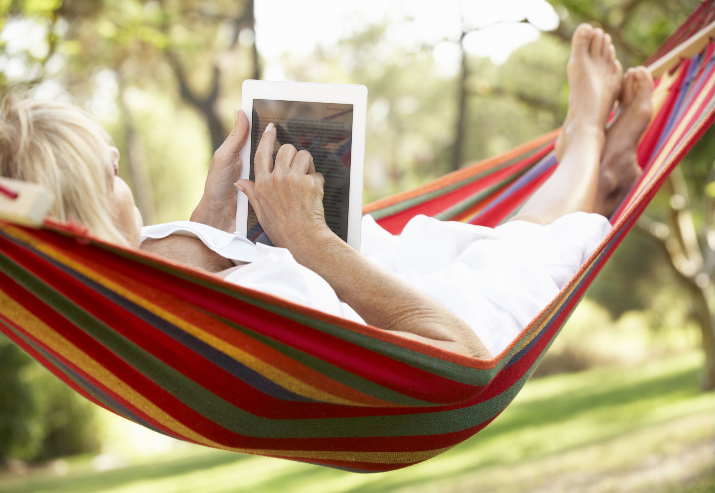 Senior Woman Relaxing In Hammock With  E-Book