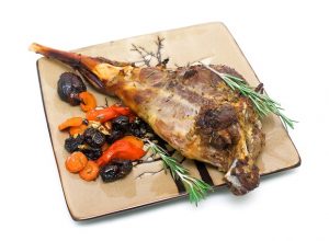 baked leg of lamb with carrots, prunes and rosemary on a plate o