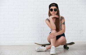 Beautiful hipster girl with skateboard on light background